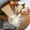 Block of Parmesan cheese on a wooden cutting board with a grater and knife.